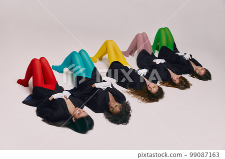 Portrait of young beautiful different women in black jackets and colored tights lying on floor over grey background. Concept of contemporary art, fashion Portrait of young beautiful different women in black jackets and colored tights lying on floor over grey background. Concept of contemporary art, fashion 99087163