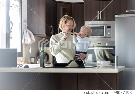 Happy mother and little infant baby boy cooking and tasting healthy dinner in domestic kitchen. Family, lifestyle, domestic life, food, healthy eating and people concept 99087198
