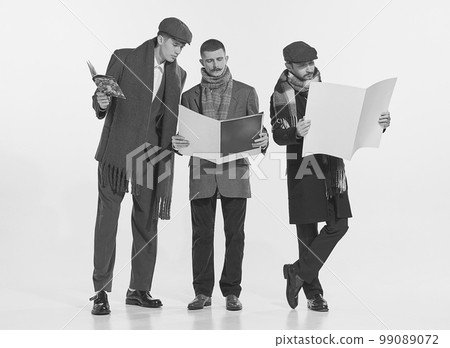 Portrait of stylish men reading magazines and newspapers isolated over grey background. Autumn male fashion 99089072