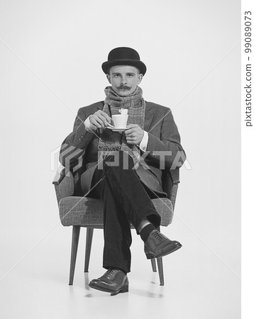 Retro man, gentlmen and detective with serious look sitting on chair and drinking coffee. Retro vintage fashion, job, professional occupationa and emotion concept 99089073