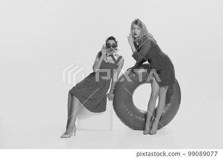 Black and white portrait of two stylish young women on cruise sitting whispering gossips. Concept of vintage fashion, travel, 70s, 80s fashion style 99089077