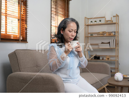 Asian old woman sipping tea in living room at home 99092413