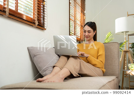 Happy Asian woman while using her laptop in the living room. work from home 99092414
