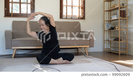 Healthy and elderly woman in workout clothes practicing yoga in her living room Healthy and elderly woman in workout clothes practicing yoga in her living room 99092609