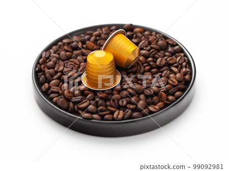 Coffee capsules suitable for machine on round plate on white with raw coffee beans. Coffee capsules suitable for machine on round plate on white with raw coffee beans. 99092981