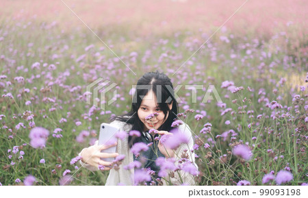 Outdoor travel asian woman using mobile phone in wild flower blossom park field 99093198