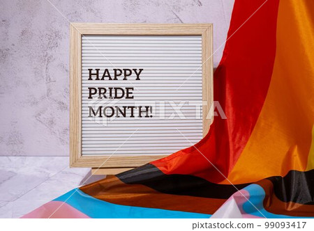 HAPPY PRIDE MONTH inscription positive quote phrase text frame on Rainbow LGBTQIA flag made from silk material. Symbol of LGBTQ pride month. Equal rights. Peace and freedom. Support LGBTQIA community 99093417