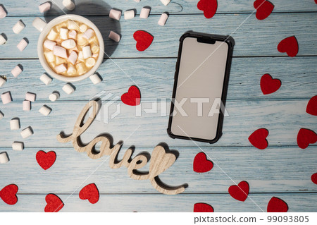 Greeting or invitation white screen on mobile phone mock up with white cup of coffee and marshmallows on wooden background. Romantic Small hearts Valentine day. Blank card copy space for your text. 99093805