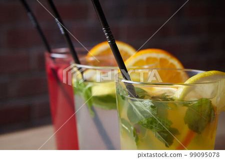 several different drinks on table, lemonade in glass, slice of lemon and straws, dark background, indoors 99095078