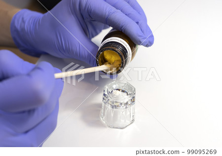 Manicurist picks some beeswax cream, paste or powder with minerals for nail from brown bottle into glass cup by orange stick. Eco Japanese manicure, beauty treatments, strengthen of nails. Horizontal Manicurist picks some beeswax cream, paste or powder with minerals for nail from brown bottle into glass cup by orange stick. Eco Japanese manicure, beauty treatments, strengthen of nails. Horizontal 99095269