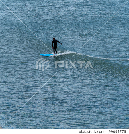 One man in a waterproof suit is surfing. Water sports. Man in black wet suit surfing on sea One man in a waterproof suit is surfing. Water sports. Man in black wet suit surfing on sea 99095776