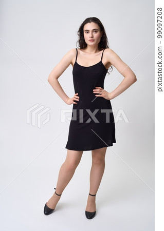 Young female model in black dress standing with hands on waist 99097208
