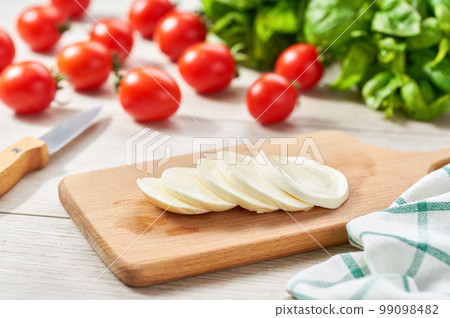 sliced Italian cheese mozzarella buffalo with cherry tomatoes and green fresh organic basil on a kitchen table. 99098482