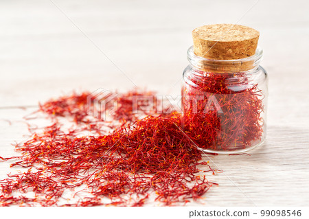 Dried saffron spices in a bottle on a wooden table, selective focus. 99098546