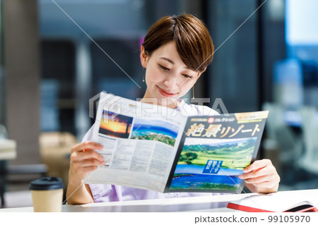 A woman looking at a travel pamphlet at a cafe Photographing cooperation: WEEK Shibadaimon (Sun Frontier Fudousan) 99105970