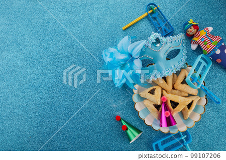 Purim celebration concept. Jewish carnival background. hamantaschen or hamans ears cookies, carnival mask and noisemaker Purim celebration concept. Jewish carnival background. hamantaschen or hamans ears cookies, carnival mask and noisemaker 99107206