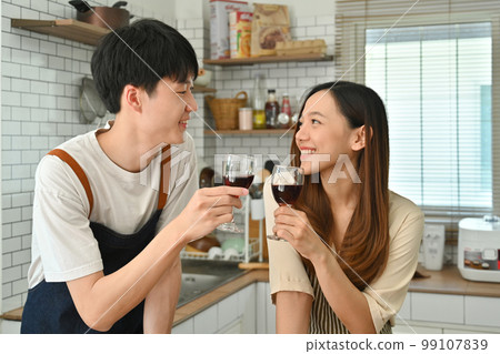 Romantic couple drinking red wine while preparing dinner in modern kitchen together 99107839
