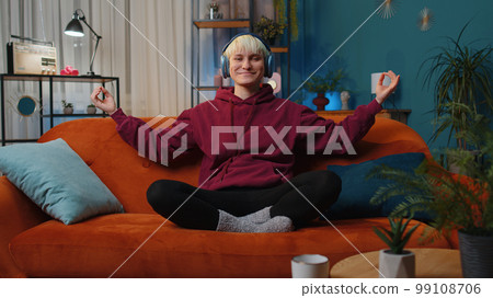 Woman with short hair at home couch eyes closed meditating with concentrated thoughts, listen music 99108706