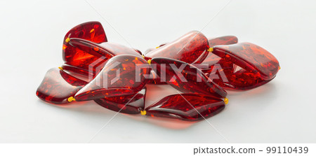 Transparent polished beads of red amber on a white background. Sun stone. Natural mineral material for jewelry. Amber texture. Copal. Ancient fossil resin 99110439