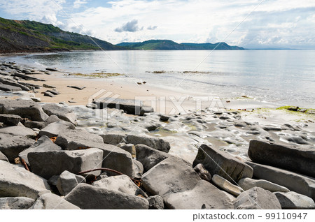 Famous Lyme Regis beach, world heritage site in Dorset, South West England. View of stones and liffs and blue sea. The beach is full of fossils. Selective focus Famous Lyme Regis beach, world heritage site in Dorset, South West England. View of stones and liffs and blue sea. The beach is full of fossils. Selective focus 99110947