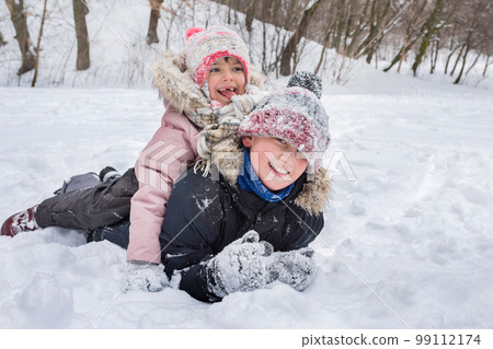 Happy children in winterwear laughing while playing in snowdrift outside. Winter childrens vacation Happy children in winterwear laughing while playing in snowdrift outside. Winter childrens vacation 99112174