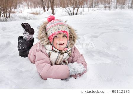 Happy little girl lies in the snow outdoors in winter Happy little girl lies in the snow outdoors in winter 99112185