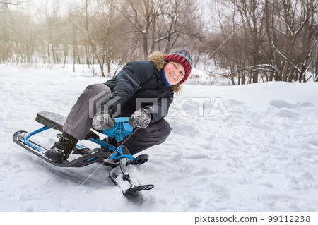 Happy boy rides a snow scooter from a mountain in the snow in winter 99112238