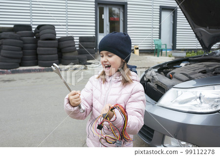 A child mechanic works in a garage, outdoors. Car repair services. Car service. A child mechanic works in a garage, outdoors. Car repair services. Car service. 99112278