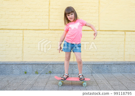 Stylish, little girl with a skateboard on a background of a yellow wall, posing for the camera Stylish, little girl with a skateboard on a background of a yellow wall, posing for the camera 99118795