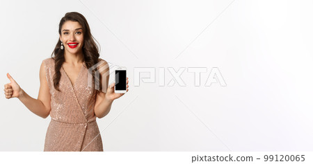 Online shopping. Beautiful young woman in party dress and makeup, showing thumbs up and mobile screen, praising good app, white background 99120065