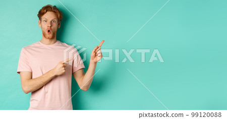 Handsome caucasian man with red hair, gasping in awe, pointing fingers at upper right corner, checking out promotion deal, standing over turquoise background 99120088