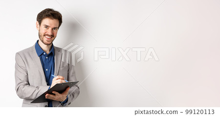 Smiling male manager in suit writing on clipboard, taking notes at office meeting, standing on white background Smiling male manager in suit writing on clipboard, taking notes at office meeting, standing on white background 99120113