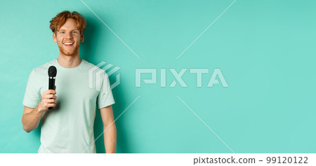 Young redhead man with beard, wearing t-shirt, holding microphone and making speech, singing karaoke, standing over mint background Young redhead man with beard, wearing t-shirt, holding microphone and making speech, singing karaoke, standing over mint background 99120122