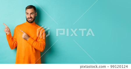Displeased man cringe from something bad, pointing and looking at something disgusting or strange, left side copy space, standing against turquoise background Displeased man cringe from something bad, pointing and looking at something disgusting or strange, left side copy space, standing against turquoise background 99120124