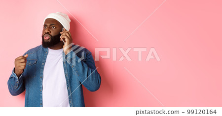 Angry african-american man talking on phone and threaten someone with raised fist, looking bothered at person, standing over pink background Angry african-american man talking on phone and threaten someone with raised fist, looking bothered at person, standing over pink background 99120164