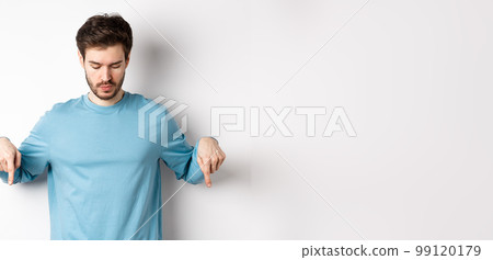 Handsome caucasian man with beard, wearing blue shirt, looking and pointing down at interesting logo banner, standing on white background Handsome caucasian man with beard, wearing blue shirt, looking and pointing down at interesting logo banner, standing on white background 99120179