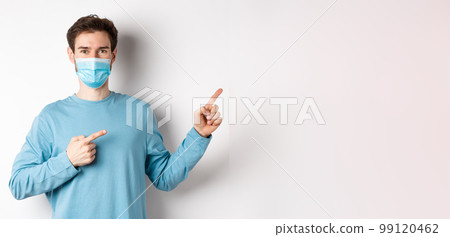 Coronavirus, health and quarantine concept. Handsome caucasian man in face mask pointing fingers right, showing advertisement, standing over white background Coronavirus, health and quarantine concept. Handsome caucasian man in face mask pointing fingers right, showing advertisement, standing over white background 99120462