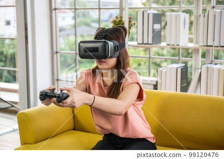 asian woman playing video games with controller with virtual glasses 99120476