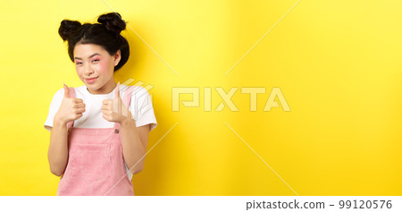 Cute teen asian girl with beauty makeup, showing thumbs up and smiling, praising and motivating you, making compliment, standing pleased on yellow background Cute teen asian girl with beauty makeup, showing thumbs up and smiling, praising and motivating you, making compliment, standing pleased on yellow background 99120576