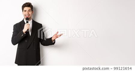 Portrait of handsome man in black suit singing a song, holding microphone and giving speech, standing against white background Portrait of handsome man in black suit singing a song, holding microphone and giving speech, standing against white background 99121654