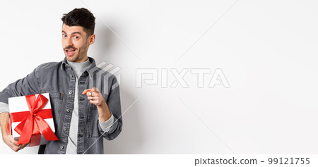 Portrait of romantic guy buying gift for Valentines day and pointing at you, inviting to special deal shopping, standing with present on white background 99121755
