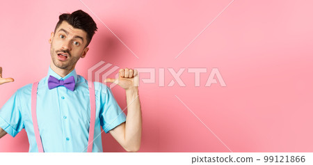 Sassy and confident young man in suspenders and bow-tie, pointing at himself and looking like professional, standing over pink background Sassy and confident young man in suspenders and bow-tie, pointing at himself and looking like professional, standing over pink background 99121866