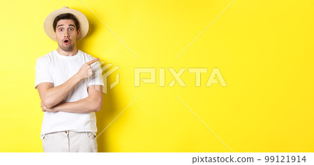 Surprised man in straw hat pointing finger right, showing promo banner, standing over yellow background 99121914