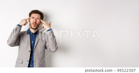 Distressed and tensed businessman pointing at head and complaining, feeling annoyed with situation blowing his mind, standing bothered on white background Distressed and tensed businessman pointing at head and complaining, feeling annoyed with situation blowing his mind, standing bothered on white background 99122307