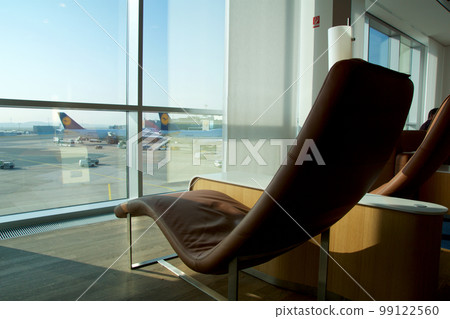 FRANKFURT, GERMANY - 11 NOV 2017: Comfortable lounge chair upholstered in light brown leather in the airport frequent flyer lounge with a view of the aircraft on the apron FRANKFURT, GERMANY - 11 NOV 2017: Comfortable lounge chair upholstered in light brown leather in the airport frequent flyer lounge with a view of the aircraft on the apron 99122560