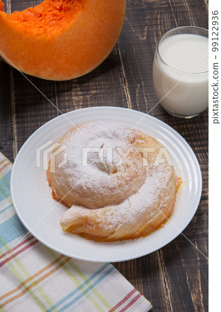 Ready-made vertuta with pumpkin lies on a plate, next to it there is a piece of pumpkin and a glass of milk 99122936