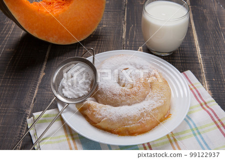 Ready-made vertuta with pumpkin lies on a plate, sprinkled with powdered sugar, next to it there is a piece of pumpkin Ready-made vertuta with pumpkin lies on a plate, sprinkled with powdered sugar, next to it there is a piece of pumpkin 99122937