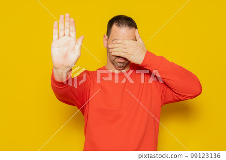 Handsome hispanic man wearing red jumper over isolated yellow background covering eyes with hands and doing stop gesture with sad and afraid expression. Embarrassed and negative concept Handsome hispanic man wearing red jumper over isolated yellow background covering eyes with hands and doing stop gesture with sad and afraid expression. Embarrassed and negative concept 99123136