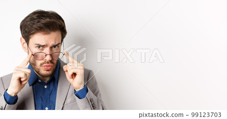 Close-up portrait of suspicious man in suit, taking-off glasses and frowning with hesitant face, standing on white background Close-up portrait of suspicious man in suit, taking-off glasses and frowning with hesitant face, standing on white background 99123703