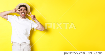 Concept of tourism and vacation. Happy man tourist posing for photo with peace signs, smiling excited, standing against yellow background Concept of tourism and vacation. Happy man tourist posing for photo with peace signs, smiling excited, standing against yellow background 99123704